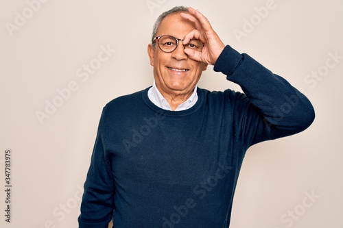 Senior handsome grey-haired man wearing sweater and glasses over isolated white background doing ok gesture with hand smiling, eye looking through fingers with happy face.