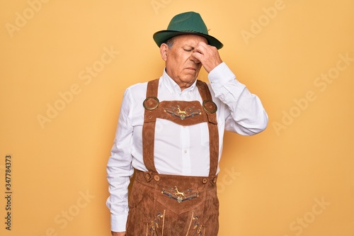 Senior grey-haired man wearing german traditional octoberfest suit over yellow background tired rubbing nose and eyes feeling fatigue and headache. Stress and frustration concept.