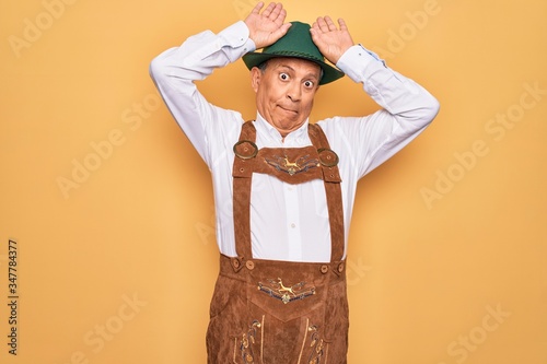 Senior grey-haired man wearing german traditional octoberfest suit over yellow background Doing bunny ears gesture with hands palms looking cynical and skeptical. Easter rabbit concept. photo
