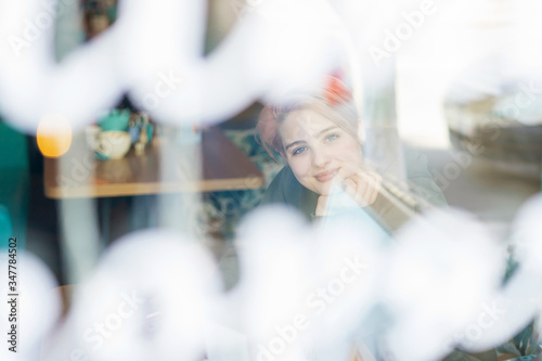 Portrait of the young girl near the building. Lifestyle. Reflections in a window. Gen Z. A young girl with pink hair sits in a cafe behind glass.