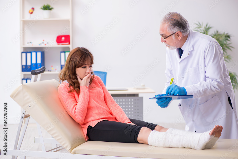 Fototapeta premium Young leg injured woman visiting old doctor traumatologist