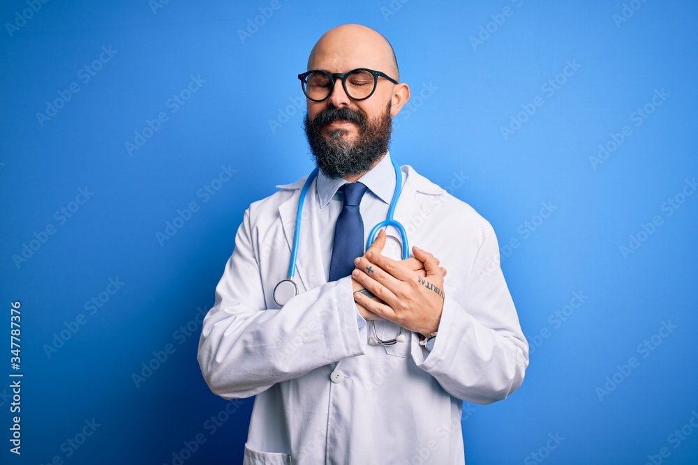 Handsome bald doctor man with beard wearing glasses and stethoscope over blue background smiling with hands on chest with closed eyes and grateful gesture on face. Health concept. Handsome bald doctor man with beard wearing glasses and stethoscope over blue background smiling with hands on chest with closed eyes and grateful gesture on face. Health concept.