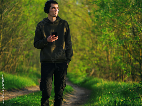 A young hipster man walks through a spring green Park and listens to music with headphones. Enjoy music and nature. Harmony