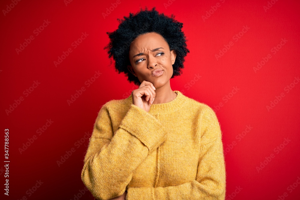 Young beautiful African American afro woman with curly hair wearing casual yellow sweater with hand on chin thinking about question, pensive expression. Smiling with thoughtful face. Doubt concept. Young beautiful African American afro woman with curly hair wearing casual yellow sweater with hand on chin thinking about question, pensive expression. Smiling with thoughtful face. Doubt concept.