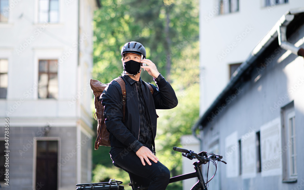 Delivery man courier with face mask and bicycle using smartphone in town.