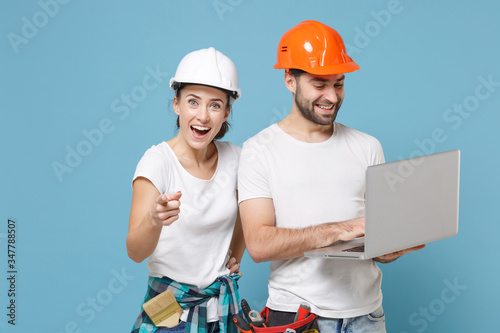 Photography Amazed couple woman man in helmet hardhat work on laptop computer isolated on blue background