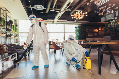 Professional workers in hazmat suits disinfecting indoor of cafe or restaurant, pandemic health risk, coronavirus photo