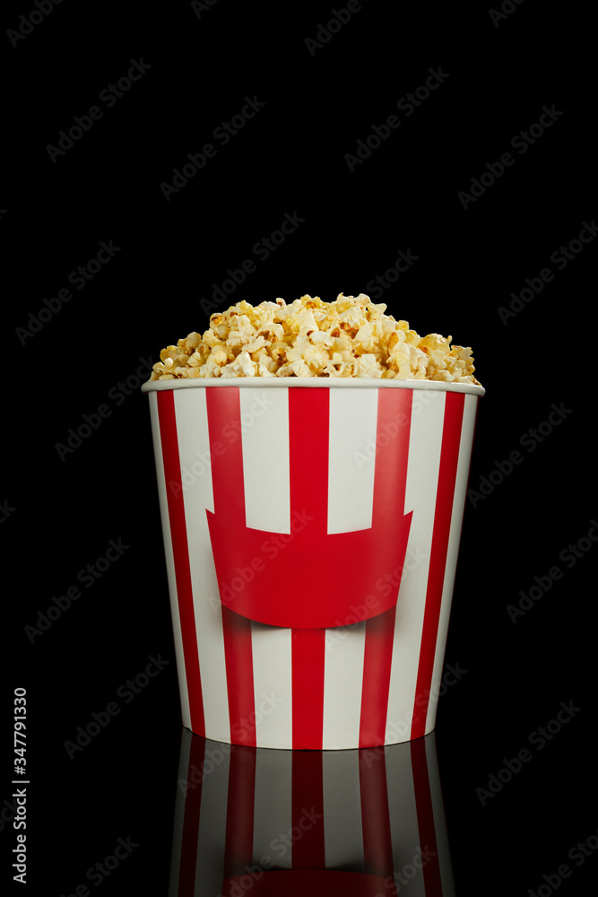 delicious fresh popcorn in classic red and white paper striped bucket isolated over the black background. delicious fresh popcorn in classic red and white paper striped bucket isolated over the black background.
