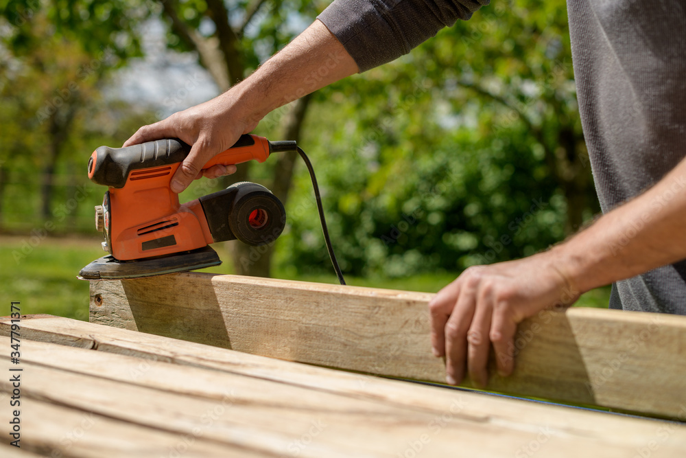 Unrecognizable man in the garden sanding wooden planks. DIY home improvement, restoration, carpentry concept. Midsection hand detail shot.