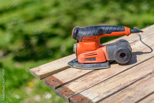 Wood sanding in the garden. DIY home improvement, restoration, carpentry concept. Close up shot of an electric sander on wooden planks. photo