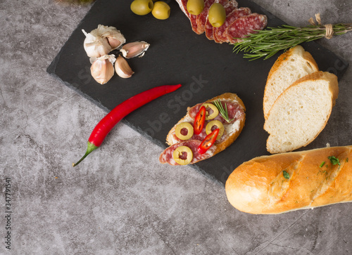 Italian bruschetta. Sandwiches with cheese and sausage, spices, chili peppers, rosemary, garlic. On a gray background and a slate board.