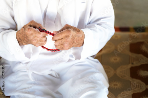 Arabic Bedouin man in traditional white holiday clothing. Close up on praying hands of an old man holding muslim rosary. Ramadhan kareem concept. photo