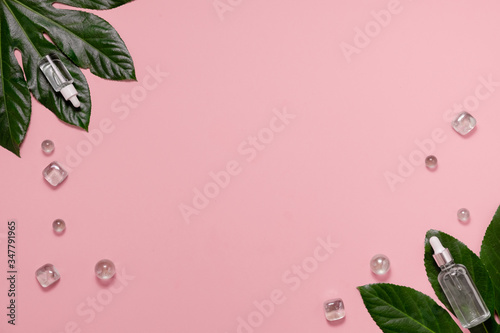 Hyaluronic acid Dropper transparant glass Bottle on pink background. Skincare and health concept. Glass bottles on tropical leaves. Top horizontal view copyspace