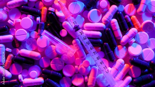 Different colorful pills and syringe rotate on white background in the neon light. The medicine concept. Multicolored medicines background.