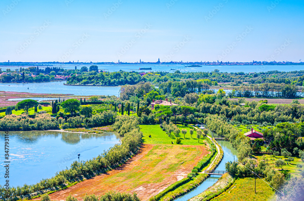 Aerial view of Torcello islands with water canal, swamp, green trees and bushes. Panoramic view of Venetian Lagoon from bell tower. Veneto Region, Northern Italy. Venice city on horizon background.
