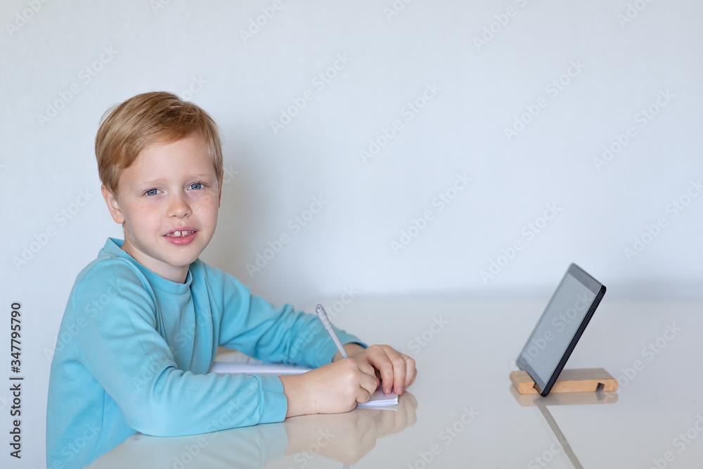 little boy using a tablet computer at distance education holds a pen looks into the frame little boy using a tablet computer at distance education holds a pen looks into the frame