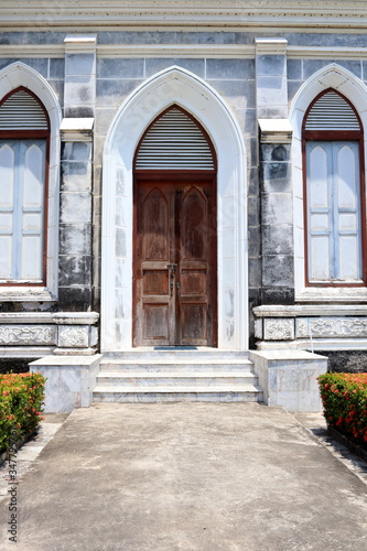 Dark brown wood door and cement way  beside of door are window. Beside of ancient church  door and windows in frame  Thailand.