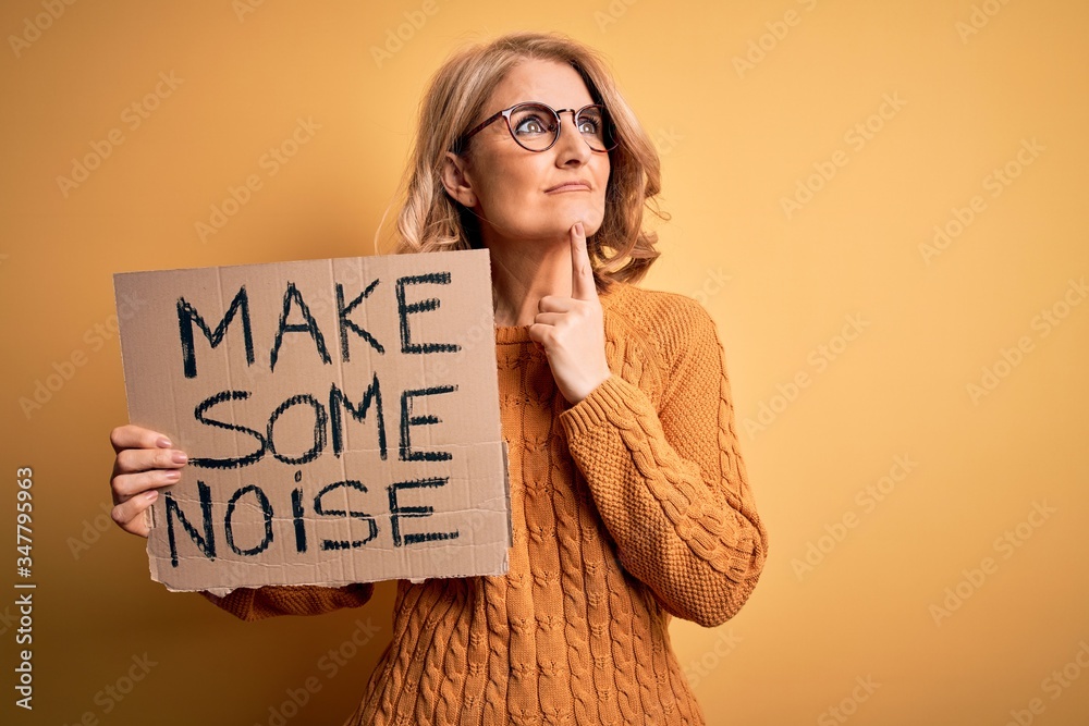 Middle age beautiful blonde activist woman holding banner with make some noise message serious face thinking about question, very confused idea Middle age beautiful blonde activist woman holding banner with make some noise message serious face thinking about question, very confused idea