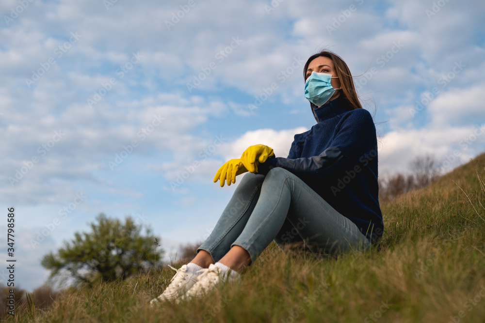 The beautiful woman in medical mask and gloves sitting on the green hill