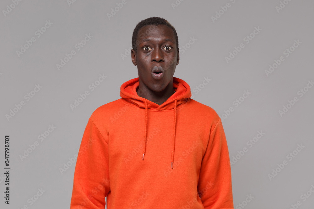 Shocked young african american man guy in orange streetwear hoodie posing isolated on grey background studio portrait. People sincere emotions, lifestyle concept. Mock up copy space. Looking camera. Shocked young african american man guy in orange streetwear hoodie posing isolated on grey background studio portrait. People sincere emotions, lifestyle concept. Mock up copy space. Looking camera.