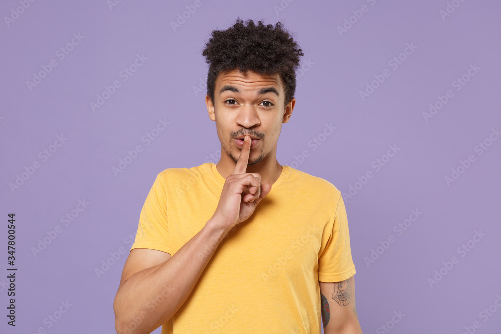 Secret young african american guy in casual yellow t-shirt posing isolated on violet background. People lifestyle concept. Mock up copy space. Saying hush be quiet with finger on lips shhh gesture. Secret young african american guy in casual yellow t-shirt posing isolated on violet background. People lifestyle concept. Mock up copy space. Saying hush be quiet with finger on lips shhh gesture.