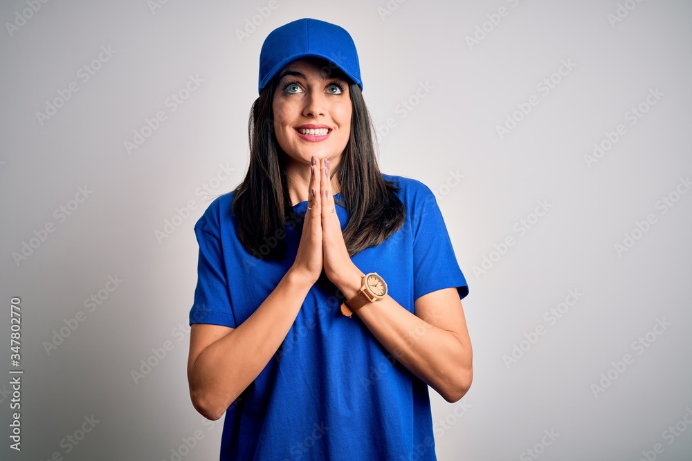 Young delivery woman with blue eyes wearing cap standing over blue background praying with hands together asking for forgiveness smiling confident. Young delivery woman with blue eyes wearing cap standing over blue background praying with hands together asking for forgiveness smiling confident.