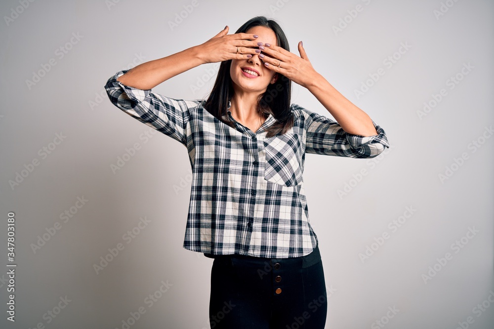 Young brunette woman with blue eyes wearing casual shirt and glasses over white background covering eyes with hands smiling cheerful and funny. Blind concept. Young brunette woman with blue eyes wearing casual shirt and glasses over white background covering eyes with hands smiling cheerful and funny. Blind concept.