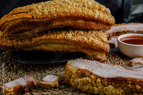 Large crispy pork on a black plate, cut into slices on a wooden chopping board with spicy sauce on a wooden table