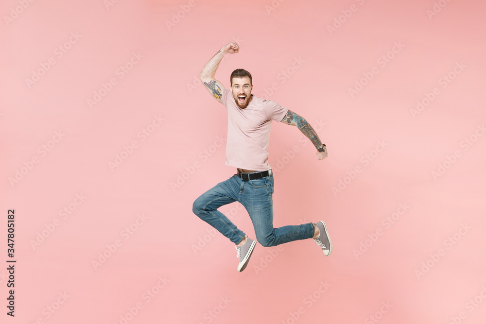 Excited young tattooed man guy in pastel casual t-shirt posing isolated on pink background studio portrait. People sincere emotions lifestyle concept. Mock up copy space. Jumping doing winner gesture.