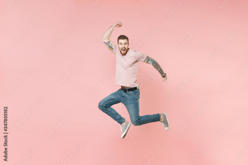 Excited young tattooed man guy in pastel casual t-shirt posing isolated on pink background studio portrait. People sincere emotions lifestyle concept. Mock up copy space. Jumping doing winner gesture. Excited young tattooed man guy in pastel casual t-shirt posing isolated on pink background studio portrait. People sincere emotions lifestyle concept. Mock up copy space. Jumping doing winner gesture.