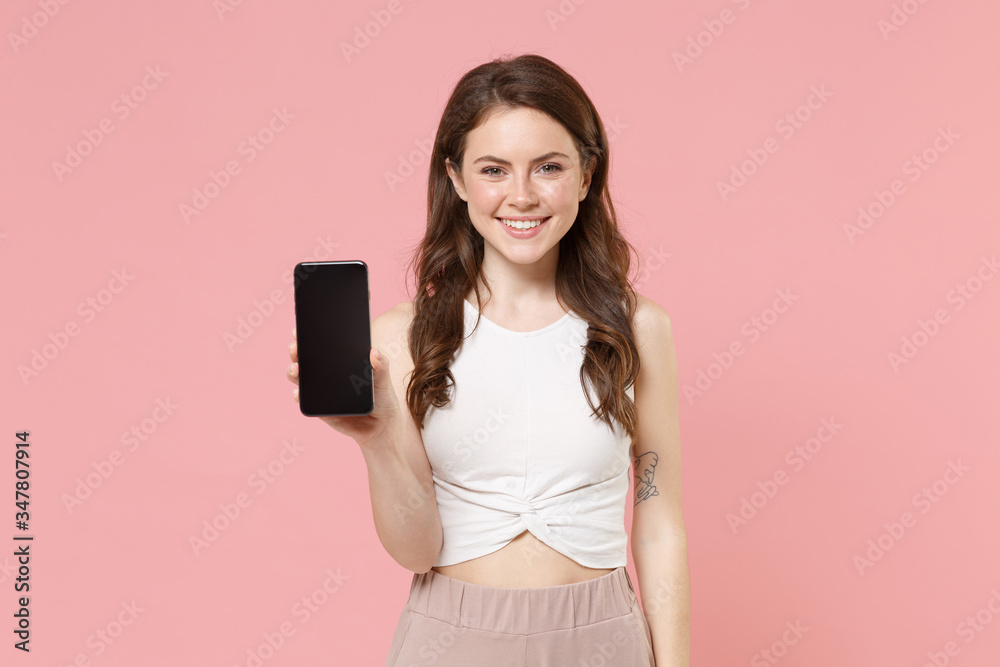 Smiling young brunette woman girl in light casual clothes posing isolated on pastel pink background studio. People lifestyle concept. Mock up copy space. Hold mobile phone with blank empty screen. Smiling young brunette woman girl in light casual clothes posing isolated on pastel pink background studio. People lifestyle concept. Mock up copy space. Hold mobile phone with blank empty screen.