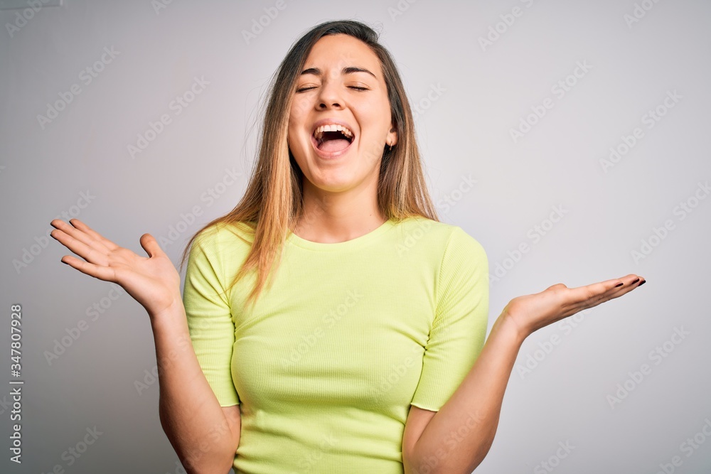 Beautiful blonde woman with blue eyes wearing green casual t-shirt over white background celebrating mad and crazy for success with arms raised and closed eyes screaming excited. Winner concept Beautiful blonde woman with blue eyes wearing green casual t-shirt over white background celebrating mad and crazy for success with arms raised and closed eyes screaming excited. Winner concept