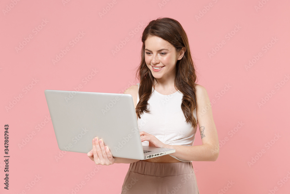 Smiling young brunette woman girl in light casual clothes posing isolated on pastel pink wall background studio portrait. People lifestyle concept. Mock up copy space. Working on laptop pc computer. Smiling young brunette woman girl in light casual clothes posing isolated on pastel pink wall background studio portrait. People lifestyle concept. Mock up copy space. Working on laptop pc computer.