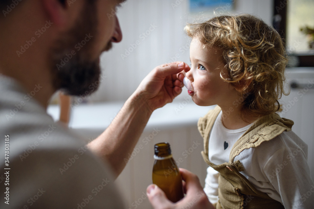 Unrecognizable father giving syrup to small sick daughter indoors at home. Unrecognizable father giving syrup to small sick daughter indoors at home.