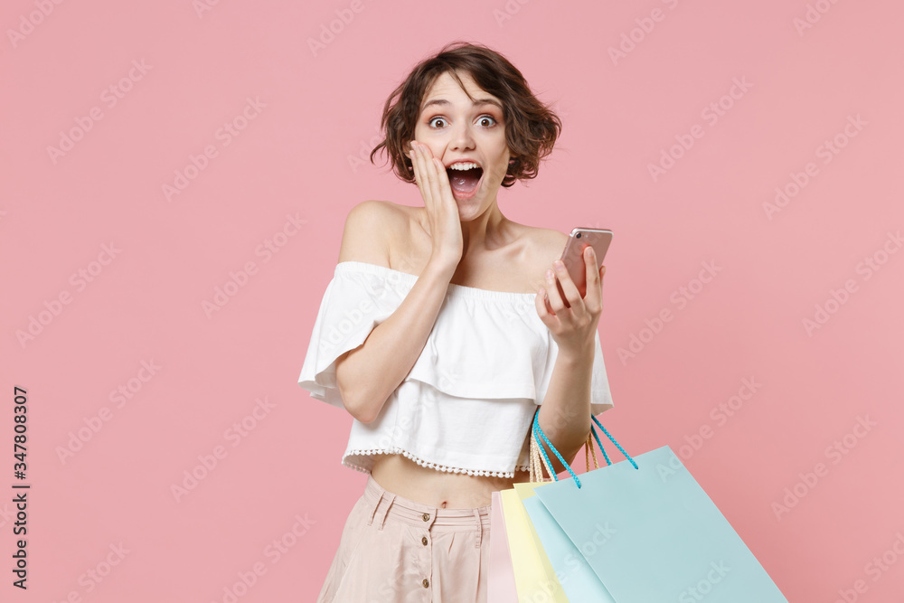 Shocked young woman girl in summer clothes hold package bag with purchases isolated on pink wall background. Shopping discount sale concept. Mock up copy space. Using mobile phone, put hand on cheek. Shocked young woman girl in summer clothes hold package bag with purchases isolated on pink wall background. Shopping discount sale concept. Mock up copy space. Using mobile phone, put hand on cheek.
