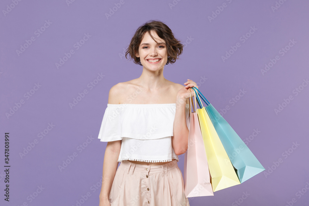 Smiling young woman girl in summer clothes hold package bag with purchases isolated on pastel violet background studio portrait. Shopping discount sale concept. Mock up copy space. Looking camera.