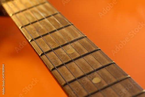 Acoustic guitar neck on an orange background. Part of a guitar on a bright background.
