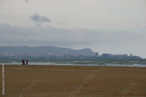 The black sea during a spring storm. The waves are rising high. Clouds hang low over the water. The deserted beach makes a grim impression. The city is visible in the haze.