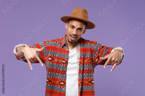 Young african american guy in casual colorful shirt hat posing isolated on violet background studio portrait. People emotions lifestyle concept. Mock up copy space. Depicting rap hip-hop YO gesture.