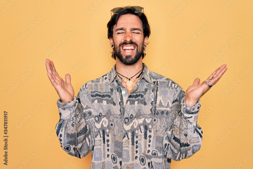 Young handsome hispanic bohemian man wearing hippie style and sunglasses celebrating mad and crazy for success with arms raised and closed eyes screaming excited. Winner concept Young handsome hispanic bohemian man wearing hippie style and sunglasses celebrating mad and crazy for success with arms raised and closed eyes screaming excited. Winner concept