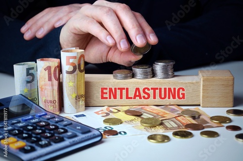 Entlastung. Männliche Hand stapelt Geld-Turm (Euro). Begriff an Baustein. Münzen, Scheine & Taschenrechner. Konzept für Business, Finanzen, Statistik