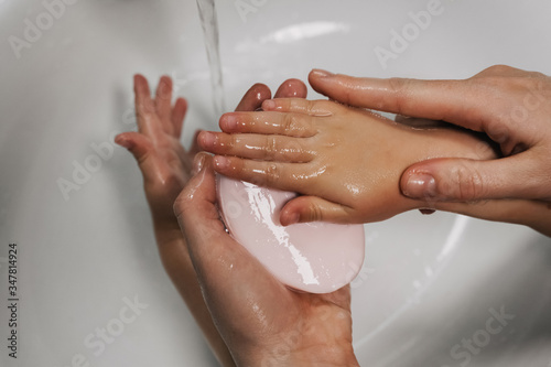 mom washes her baby's hands thoroughly with soap and foam in the bathroom for hygiene purposes, hands closeup