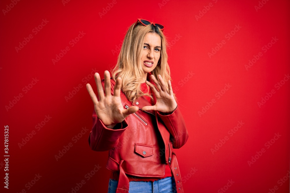 Young beautiful blonde woman wearing casual jacket standing over isolated red background disgusted expression, displeased and fearful doing disgust face because aversion reaction. With hands raised Young beautiful blonde woman wearing casual jacket standing over isolated red background disgusted expression, displeased and fearful doing disgust face because aversion reaction. With hands raised