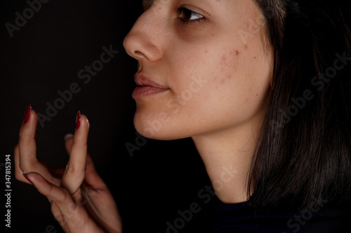 Close-up of young woman applying concealer on her face.