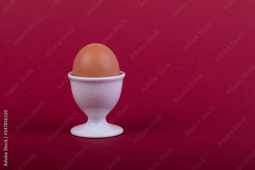 one brown egg in white egg cup before red background one brown egg in white egg cup before red background