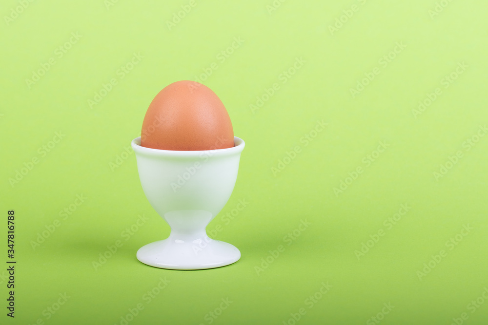 one brown egg in white egg cup before green background