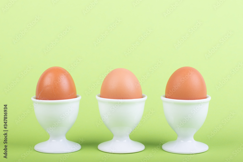 three brown eggs in white eggs cups before green background three brown eggs in white eggs cups before green background