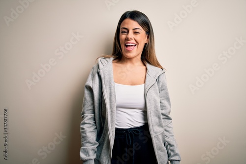Young beautiful brunette sportswoman wearing sportswoman training over white background winking looking at the camera with sexy expression, cheerful and happy face. © Krakenimages.com