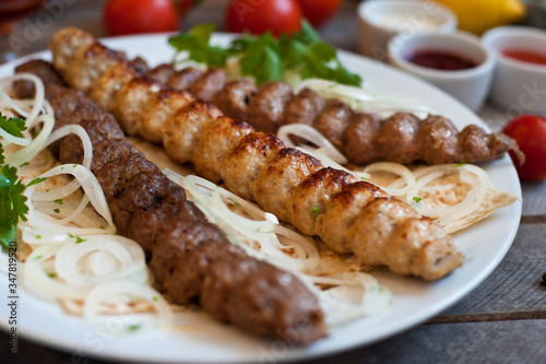 A portion of Lule kebab on a white plate with greens. A delicious dish on a brown wooden table. 