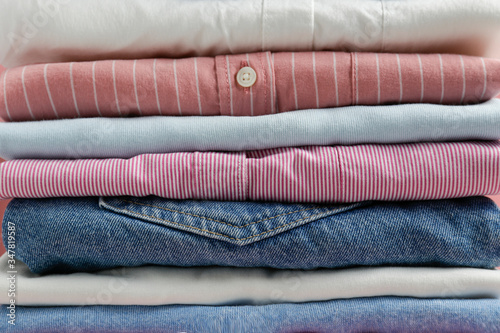 Cropped image with stack of colorful perfectly folded clothing items. Macro shot of pile of different pastel color shirts, sweaters & pants. Close up, copy space, background.